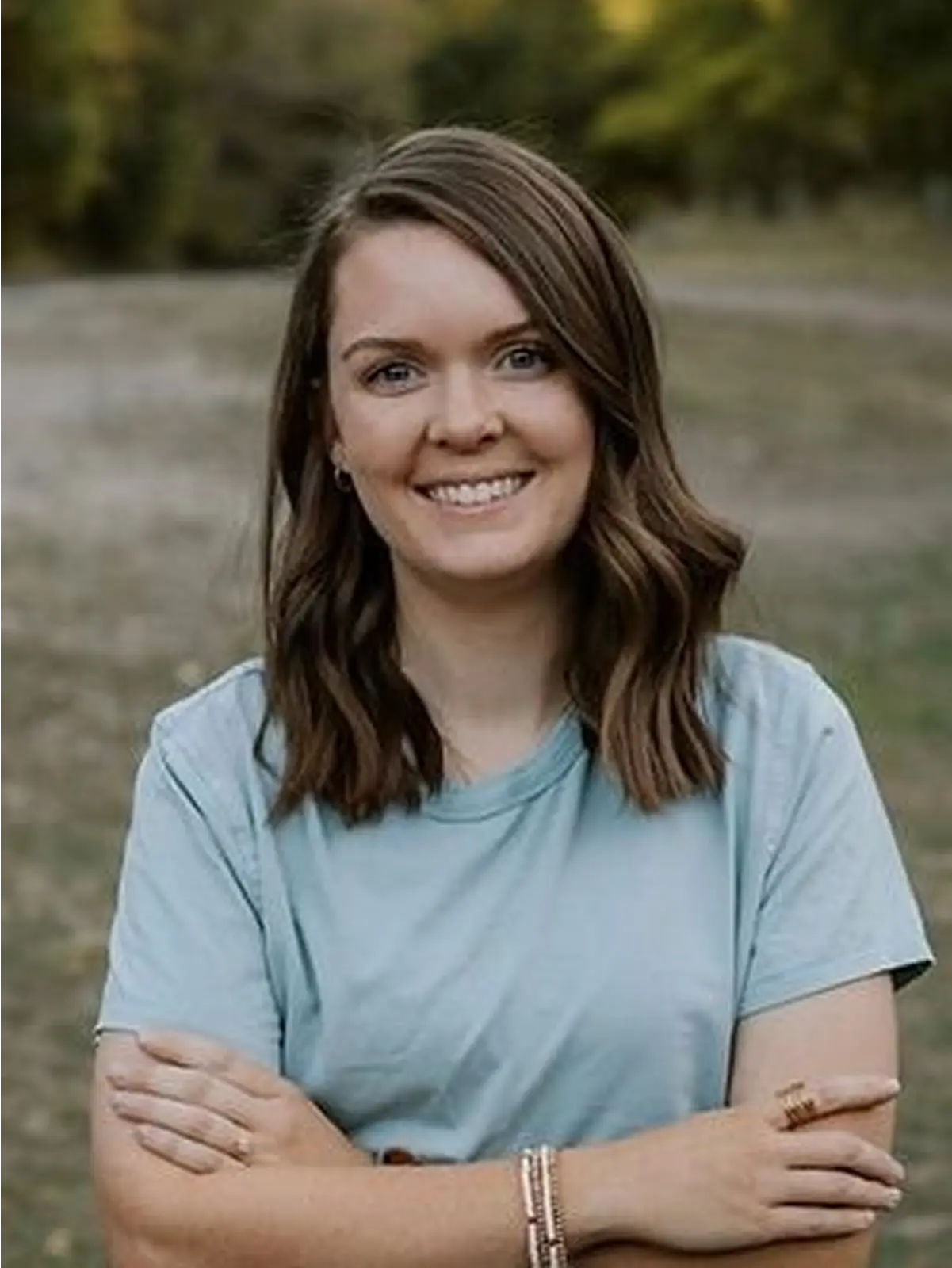 Smiling woman outdoors with crossed arms.